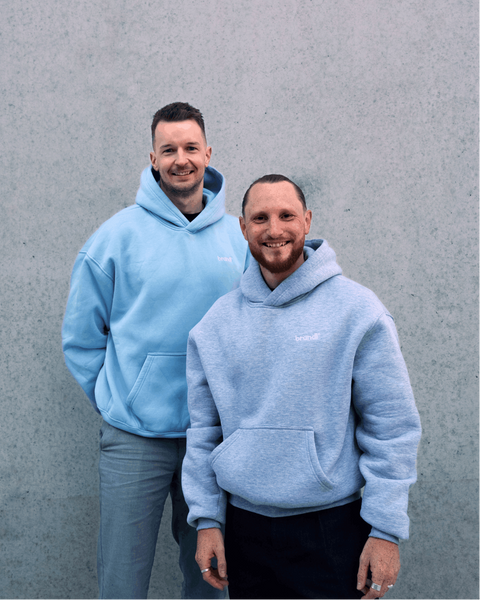 Zwei Männer, die passende hellblaue und heidegraue Hoodies mit Vordertaschen tragen.