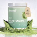 Ein mattgrüner zylindrischer behälter von brandl bio gerstengras pulver mit weißem deckel und beige etikett bio qualität