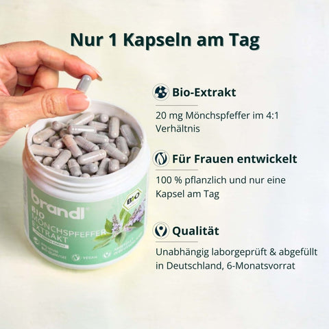Eine hand hält eine einzelne graue transparente kapsel über einem offenen weißen gefäß mit beauty & balance bundle kapseln
