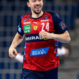 Rotes und marineblaues Handballtrikot mit weißer Nummer 24, mit Sponsorenlogos einschließlich Puma, BGVA und anderen.