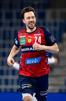 Rotes und marineblaues Handballtrikot mit weißer Nummer 24, mit Sponsorenlogos einschließlich Puma, BGVA und anderen.