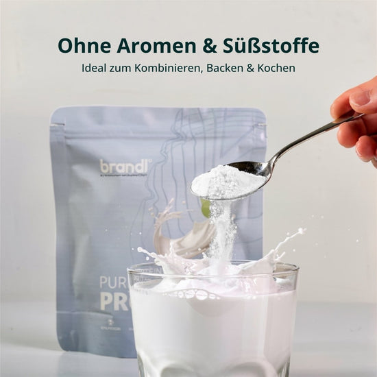 Ein löffel weißes pulver wird in ein glas milch gegeben mit dem brandl silver pouch von pure protein 2.0 vegan