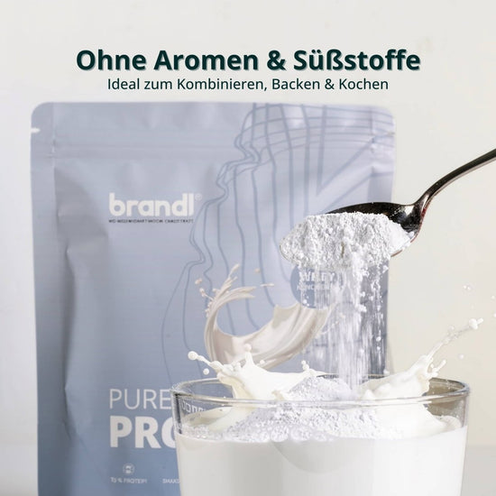 Ein schlanker silberlöffel hält eine menge weißes whey-proteinpulver pure protein 2.0 über einem glas cremiger milch